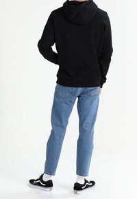 Svart huvtröja, blå jeans, svart och vit sneakers. Enkel design, blandning av bomullstextur, avslappnad passform och inga synliga logotyper eller mönster.