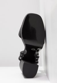 Černý vysoký podpatek s hladkým syntetickým svrškem, s texturovanou, vroubkovanou podrážkou a širokými kotníkovými pásky pro lepší podporu.