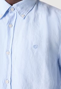 Chemise bleu clair à boutons avec col boutonné et petit logo brodé sur la poitrine gauche.