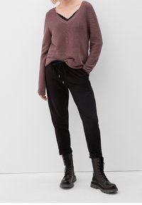 Pull col en V mauve à finition texturée superposé à un haut noir orné de dentelle, associé à un pantalon jogger noir et des bottes noires à lacets.