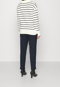 Gestreifter Strickpullover in Creme und Marineblau, kombiniert mit marineblauen schmalen Hosen. Sichtbare schwarze Stiefeletten mit Absatz und umgekrempelten Hosenbeinen.