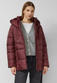 Bordeauxrode pufferjas met capuchon, met een doorgestikte textuur, zijzakken en verstelbare koordjes. Draag het over een grijze cardigan en een spijkerbroek.