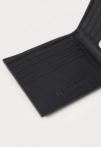 Portafoglio in pelle nera con slot per carte verticali, logo impresso e design pulito. Presenta una texture liscia e dettagli di cucitura precisi.