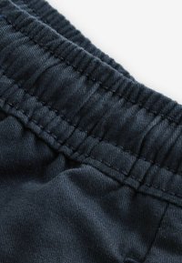 Mørkeblå stof med synlig søm, der viser en sammensamlet elastisk talje og blød tekstur. Nærbillede af materialet.