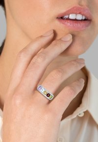 Rektangulær sølvringe med fem multifarvede ædelsten: lilla, blå, gul, rød og grøn, sat i en poleret fatning.