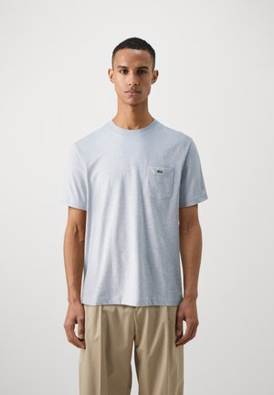 Helles graues Baumwoll-T-Shirt mit Rundhalsausschnitt, kurzen Ärmeln und einer linken Brusttasche, die ein Logo zeigt. Weiche Textur, normale Passform.