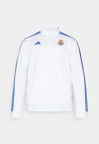 Hvit sportsjakke med blå striper, høy krage, hel glidelås og Real Madrid-logo på venstre bryst. Laget av lett materiale.