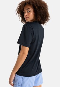 Camiseta negra de manga corta exhibida en un ángulo, hecha de una tela suave. Diseño sencillo con un corte clásico y sin patrones visibles.