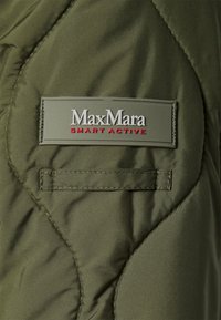 Oliven grøn quilted jakke med et gråt mærke med "MaxMara SMART ACTIVE" i hvid og rød tekst; inkluderer en lille patchlomme.