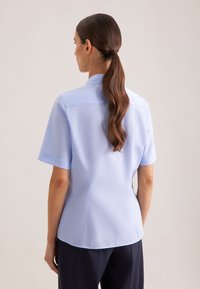 Camicia azzurro chiaro a maniche corte con colletto strutturato, texture liscia e vestibilità su misura. Sul retro presenta una cucitura per un aspetto raffinato.