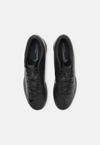 Fekete sportcipők textúrált felülettel, türkiz színű kiegészítőkkel, kerek orral, fűzős kivitelben, és Nike logóval a talpbetéten.