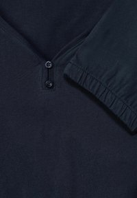 Mörkblå tröja med V-hals, två knappar och sammanknipna ärmslut. Tillverkad av mjukt, sträckt tyg.