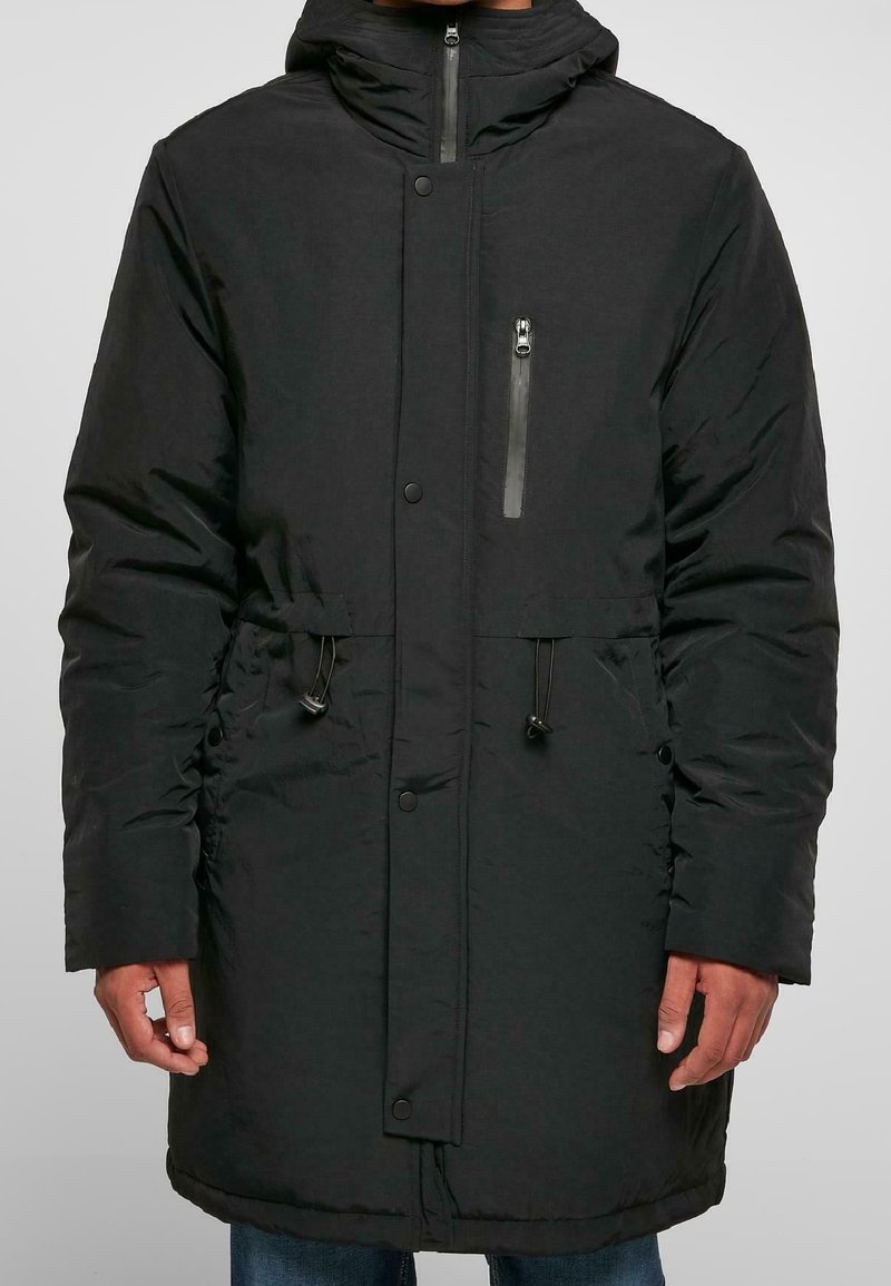 Černá zateplená parka se zipovou kapsou na hrudi, stahovacími šňůrkami v pase a knoflíkovým zapínáním. Disponuje kapucí a texturovanou tkaninou.