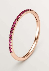 Anillo de oro rosado con una banda delgada que presenta una línea de pequeñas gemas redondas de color rosa engastadas en el borde exterior, textura suave y superficie brillante.
