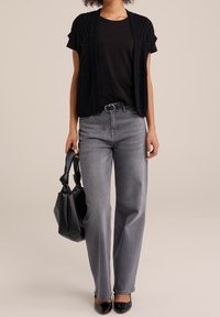 Cárdigan negro de punto sobre una camiseta negra, combinado con jeans gris de tiro alto y bailarina negra. Bolsa tote negra en la mano.