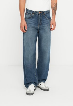 Lyseblå vide jeans laget av denim, med fem-lommedesign, knappelukk og detaljer i oransjefarge. Kombinert med hvite og grå joggesko.