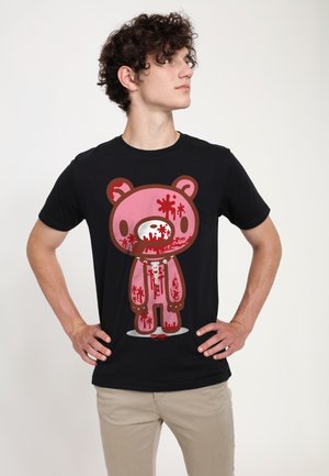 Ung mand med krøllet hår iført en sort T-shirt med en stor pink bamse grafik med røde malingstænk på.