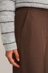 Rudos kelnes su šoninėmis kišenėmis ir lygiu paviršiumi, derinamos su šviesiai pilku dryžuotu megztiniu, turinčiu raukinių rankogalius.