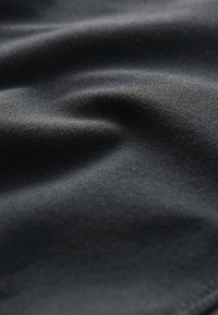 Gros plan d’un tissu sombre et lisse avec des plis subtils et une texture douce visible sous un éclairage tamisé.