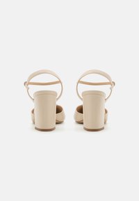 Beige klacksandaler med öppen baksida, justerbart ankelband, slät yta och fyrkantig tådesign.