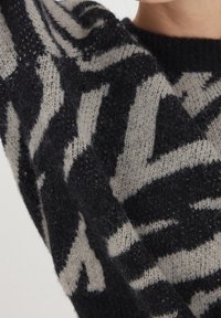 Stickad tröja med ett svart och elfenbensfärgat zigzag-mönster, tillverkad av mjukt, spöklikt material med ribbat nacke och ärmslut.