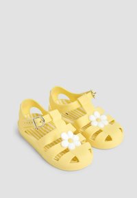 Sandale galbene din cauciuc cu un design cu bretele, având accente de flori albe pe degetul piciorului. Tălpic texturat cu model stripe.