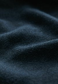 Temno modra tkanina z mehko, teksturirano površino. Material prikazuje subtilne valove in gube, ki poudarjajo njegovo prijetno kvaliteto.