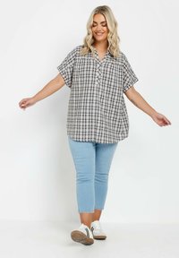 Camicetta a maniche corte, con bottoni, in un motivo a quadri marrone e bianco; tessuto leggero con una vestibilità comoda. Abbinata a jeans azzurri, lunghi fino alla caviglia.