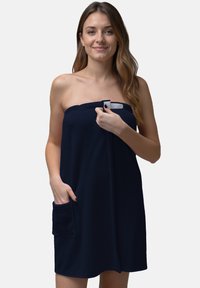 Abito in morbido tessuto di spugna blu navy con superficie testurizzata, dotato di chiusura a spilla sulla spalla e tasca laterale. Lunghezza a metà coscia e design senza spalline.