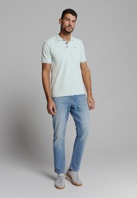 Lichtblauw poloshirt met korte mouwen en een twee-knopen placket, gecombineerd met lichtblauwe jeans en grijze sneakers met tan accenten.