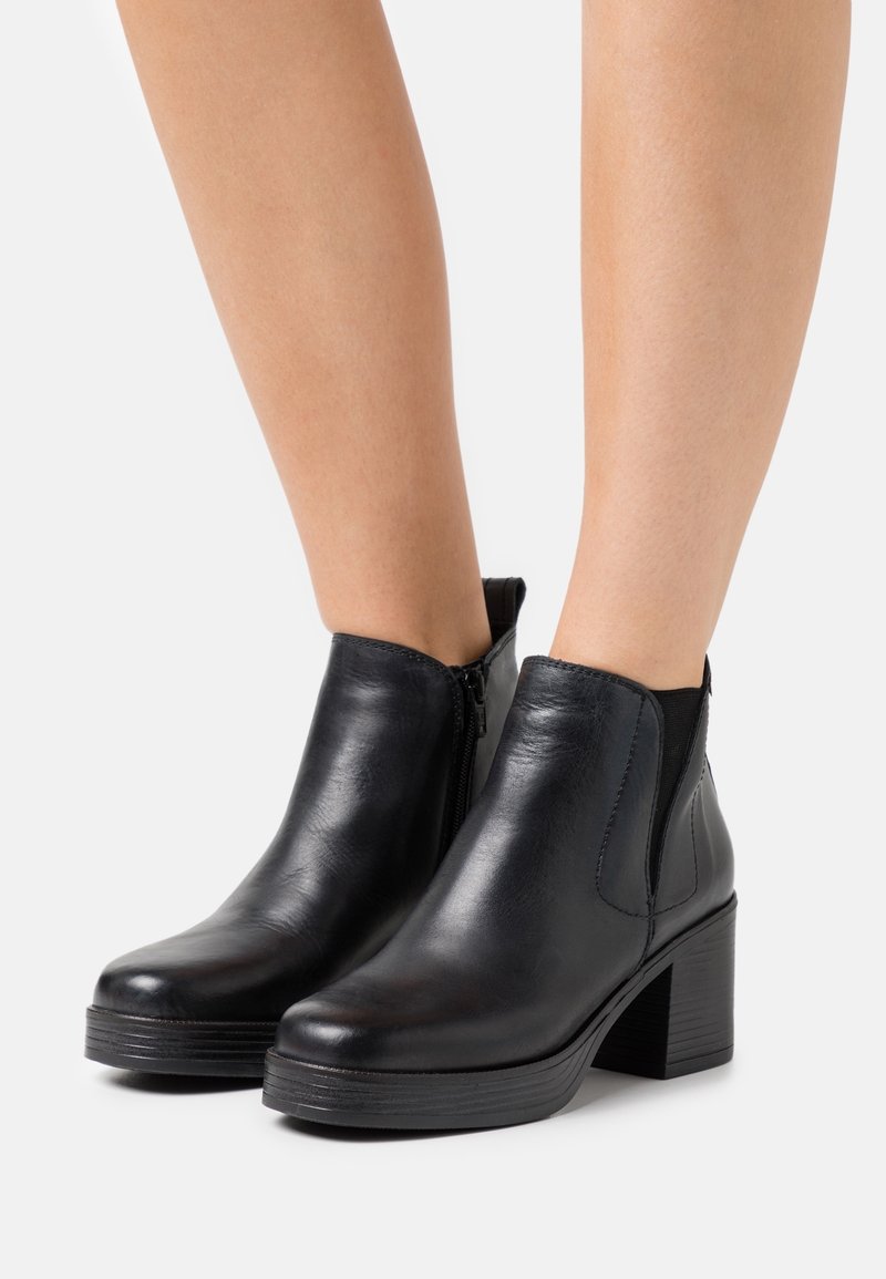 Bottines en cuir noir avec un talon épais, dotées de fermetures éclair latérales et d'accents élastiques pour un enfilage facile. Texture lisse, design classique.