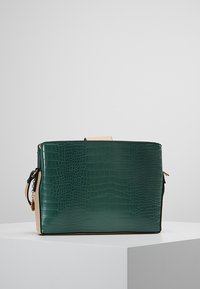 Borsa in pelle sintetica verde a forma rettangolare, con accenti in un leggero color beige chiaro e manico superiore. Presenta una chiusura con zip e una tracolla laterale.