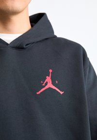 Mørkeblå hættetrøje med en blød tekstur, der har et fremtrædende pink Jumpman-logo og "A R"-tekst i fed skrift på brystområdet.