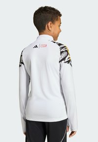 Valkoinen pitkähihainen urheilupaita, jossa mustat ja keltaiset kuvioidut korostukset olkapäillä, ja Adidas- sekä Marvel-logot takana.