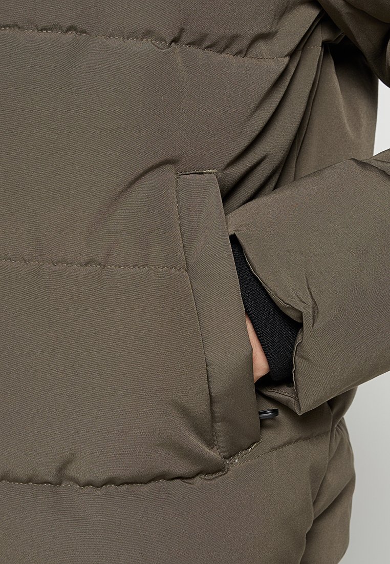 Olivgrüne isolierte Jacke mit glatter, matter Oberfläche, ausgestattet mit einer Seitentasche und schwarzen elastischen Bündchen. Strukturiertes Gewebe mit genähten Nähten.