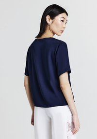 Maglietta blu navy a maniche corte realizzata in tessuto morbido, con design semplice e orlo dritto, abbinata a pantaloni bianchi con dettagli in pizzo.