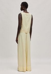 Lichtgele mouwloze top met een gladde textuur, gecombineerd met wijde broekspijpen in dezelfde kleur. Eenvoudig ontwerp, zonder patronen of versieringen.