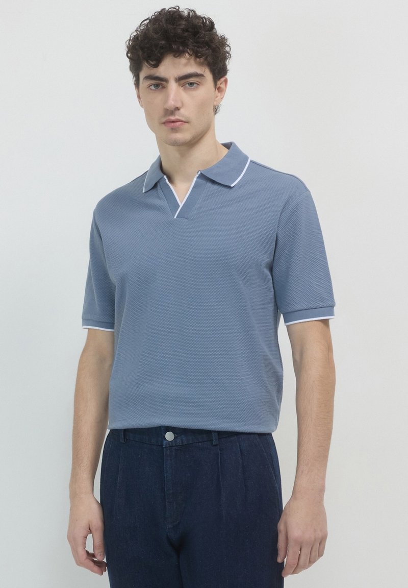 Polo shirt à manches courtes en tissu léger bleu texturé avec un col en V et un bord blanc contrastant. Assorti à un pantalon bleu foncé.