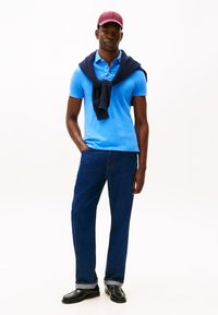 Blå polo skjorte, marineblå genser knyttet rundt halsen, mørkeblå jeans, svarte loafers og en burgunder cap. Enkel design og avslappet passform.