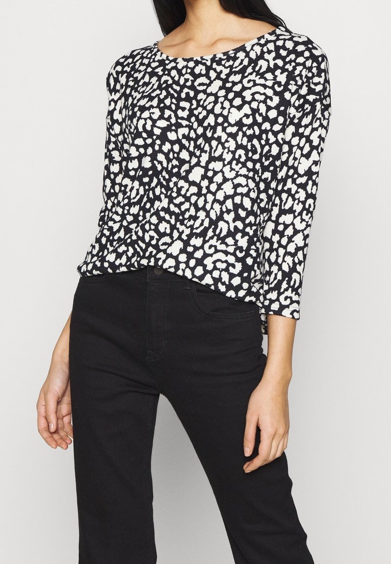Långärmad topp i svart med ett vitt djurmönster, med rundad halsringning och mjukt, strukturerat tyg. Kombinerad med svarta byxor.