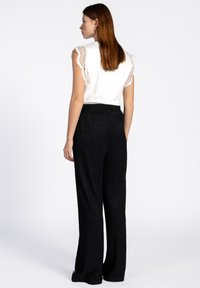 Witte top met kantafwerking bij de schouders en zwarte gestructureerde wijde broek. De outfit heeft een relaxte pasvorm en een elastische tailleband.