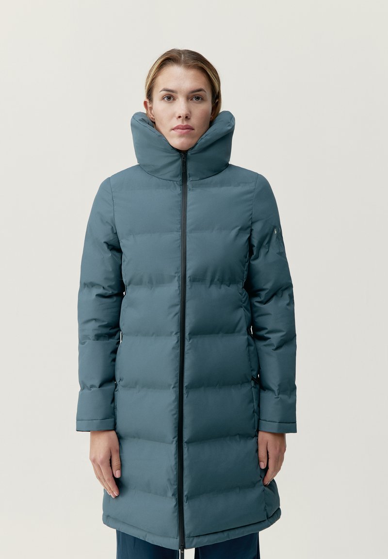 Vadderad kappa i skifferblått, med hög krage, framzipper, sidofickor och slät yta. Längden når till mitten av låret.