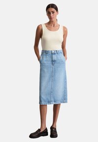 Lichte blauwe denim midi-jurk met zijzakken, een rechte snit en een knoopsluiting bij de taille. Gepaarde met een beige tanktop en donkere schoenen.