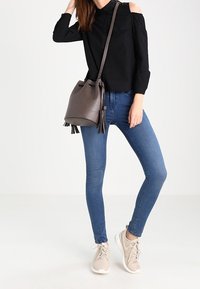 Harmaa ämpärilaukku, jossa on nyörilukko ja hapsukoristeet, musta kylmät olkapäät paljastava paita ja siniset istuvat farkut. Beiget tennarit viimeistelevät asun.