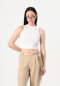 Hvit ribbestrikket crop-top med høy hals. Kombinert med beige høyt midje bukser med knytebelte og folder.