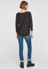 Zwart lange mouwen bovenstuk met een brede halslijn, gecombineerd met blauwe denim jeans met opgerolde manchetten en zwarte enkellaarsjes met studs.