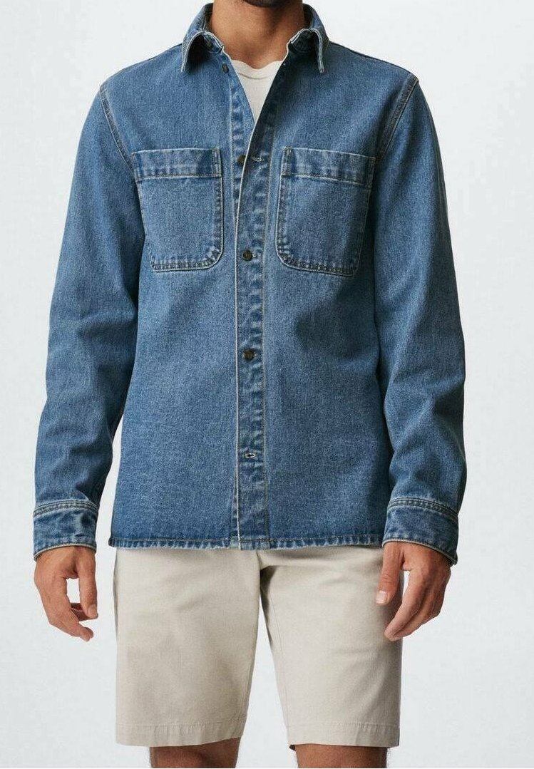 Personne portant une chemise en jean bleu à boutons avec deux poches poitrine et un short beige, debout devant un fond clair.