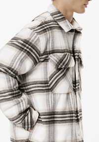 Camicia di flanella a quadri in bianco, nero e grigio. Presenta chiusura con bottoni sul davanti, due tasche sul petto e un colletto. Texture morbida e vestibilità comoda.