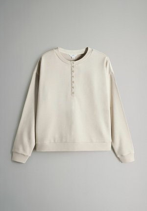 Smėlinės spalvos džemperis iš minkštos medžiagos, su apvalia iškirpte, ilgomis rankovėmis ir priekine sagų juostele su penkiomis sagomis.