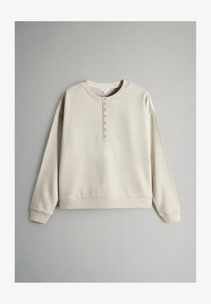 Beežist pehmest materjalist dressipluus, millel on ümmargune kaelus, pikad varrukad ja ees viie nupuga nööbitav klapp.